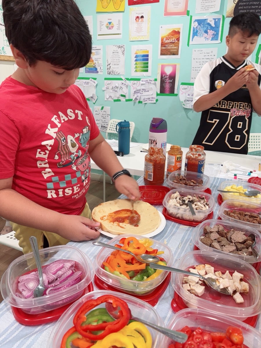 A student spreading tomato sauce across his pizza base with a spoon