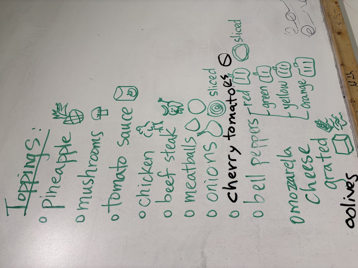 A whiteboard listing pizza toppings in green marker with a small drawing beside each one