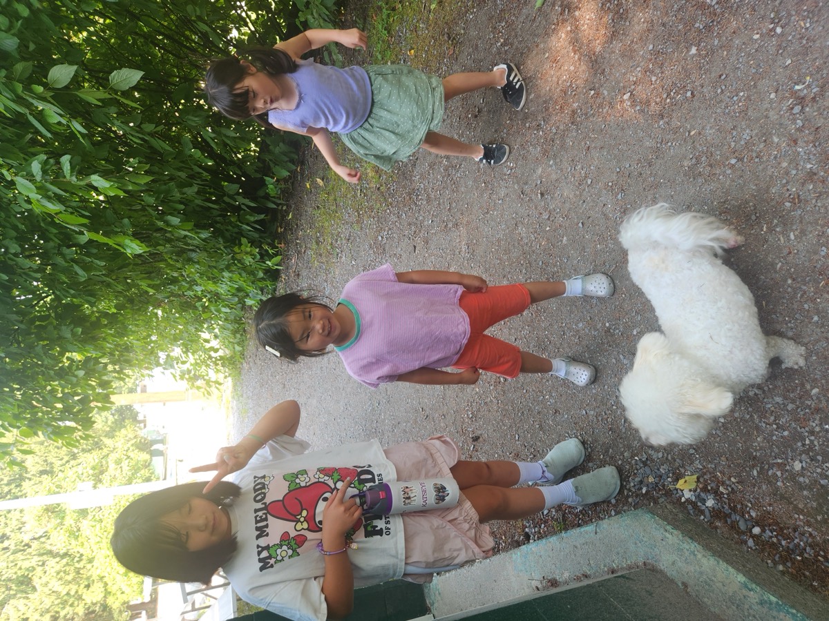 Three young campers walking along a leafy path with a small white dog