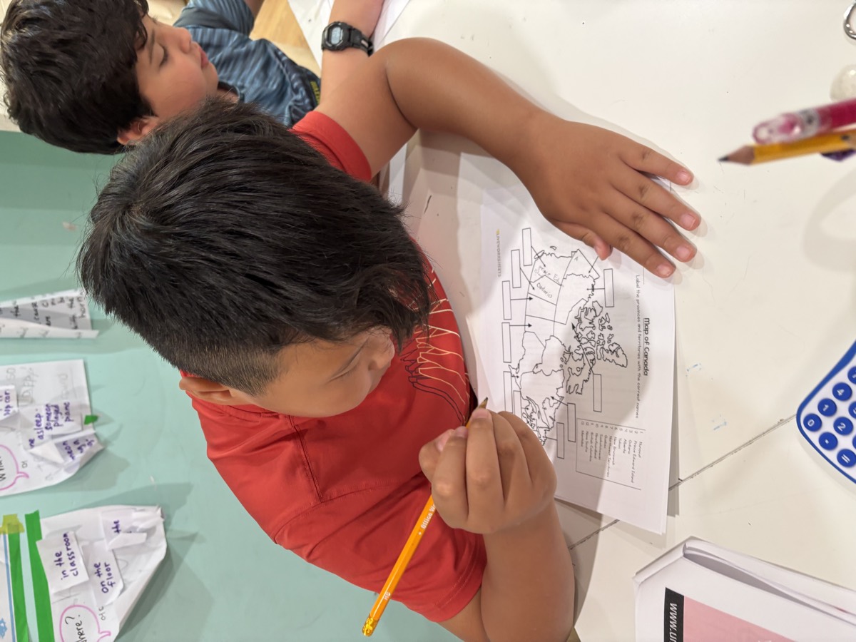 A student in a red shirt carefully filling in his map of Canada