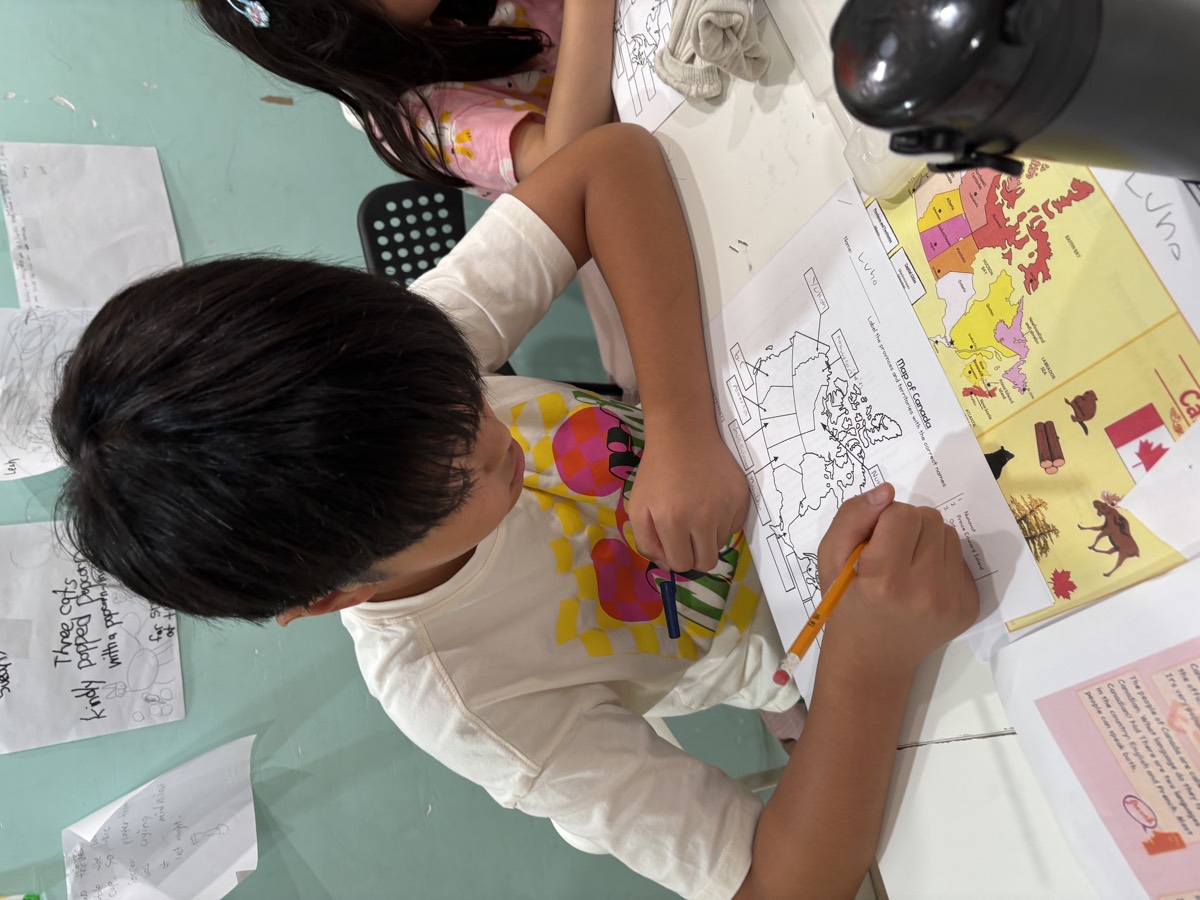 A student labelling his map with a coloured reference sheet beside him