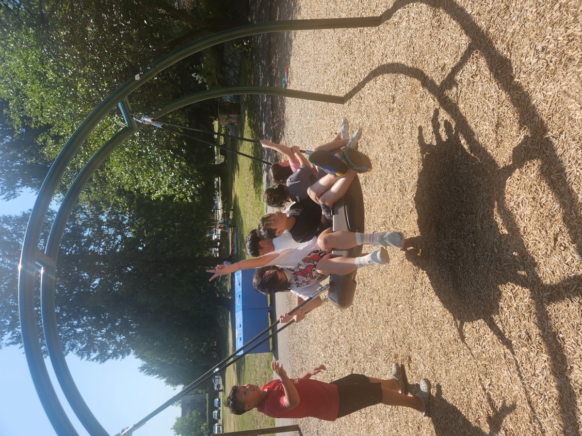 Children piled onto a large basket swing at the playground while a friend pushes