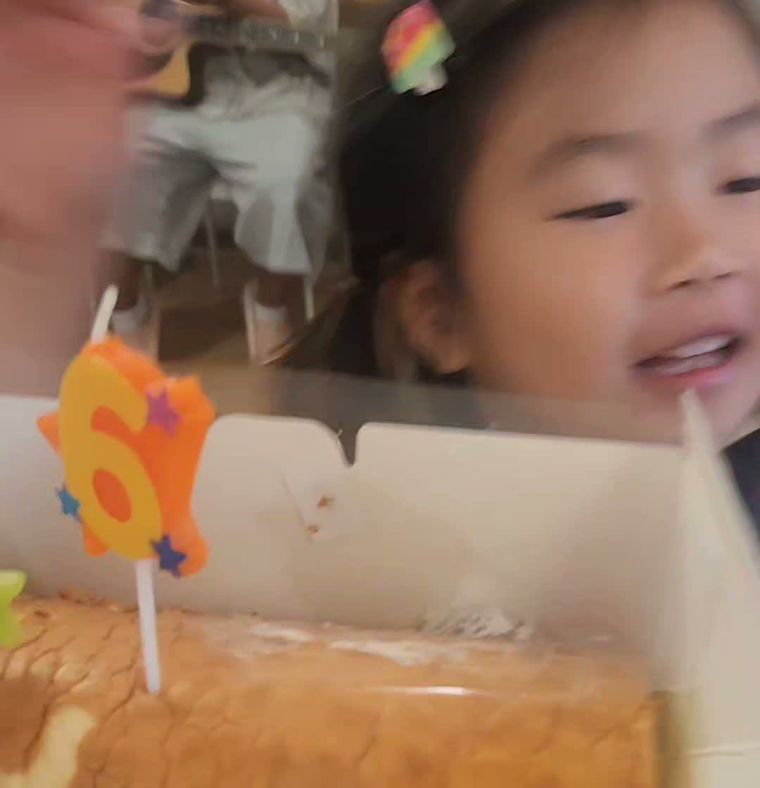 A young student smiling behind a roll cake with a number six candle on top