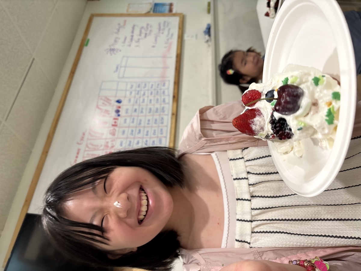 A student laughing as she holds up her plate of whipped cream and berries