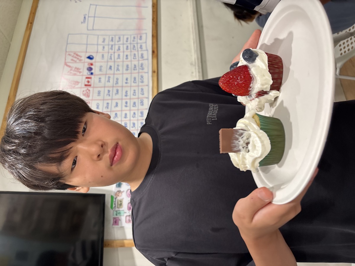 A student holding a plate with two decorated cupcakes topped with cream and berries
