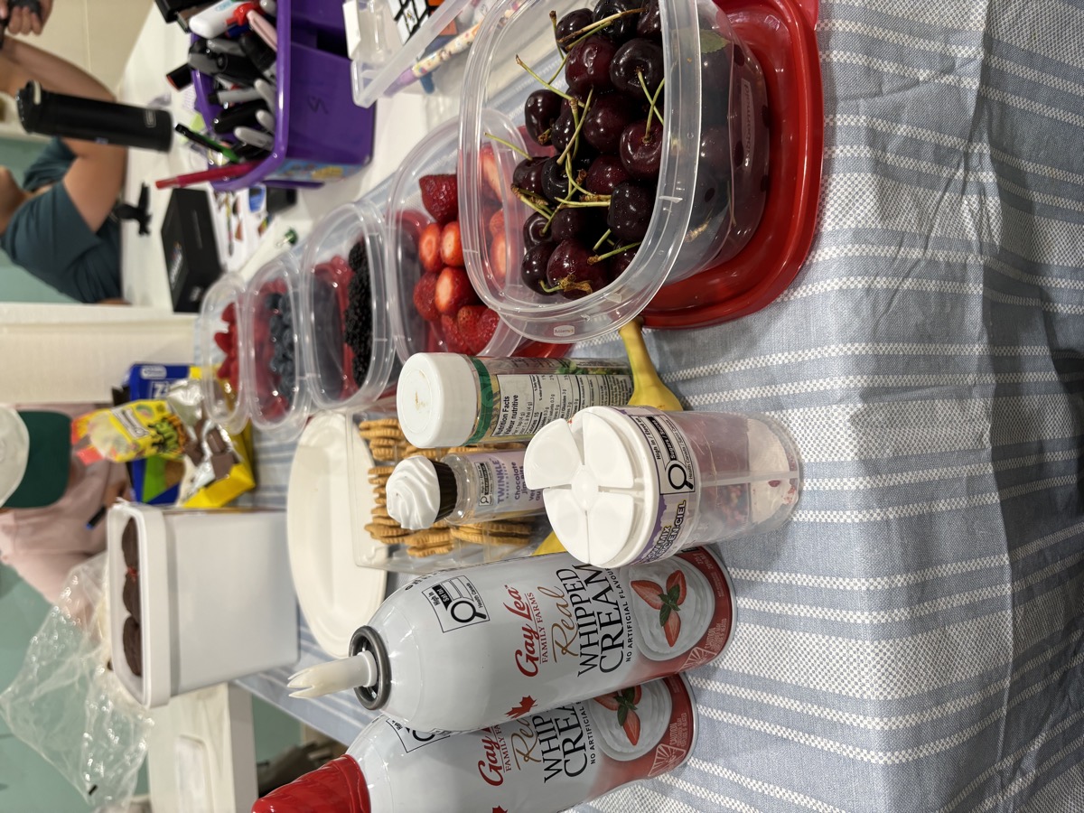 A long table covered in whipped cream cans, cupcakes and containers of fresh berries and cherries