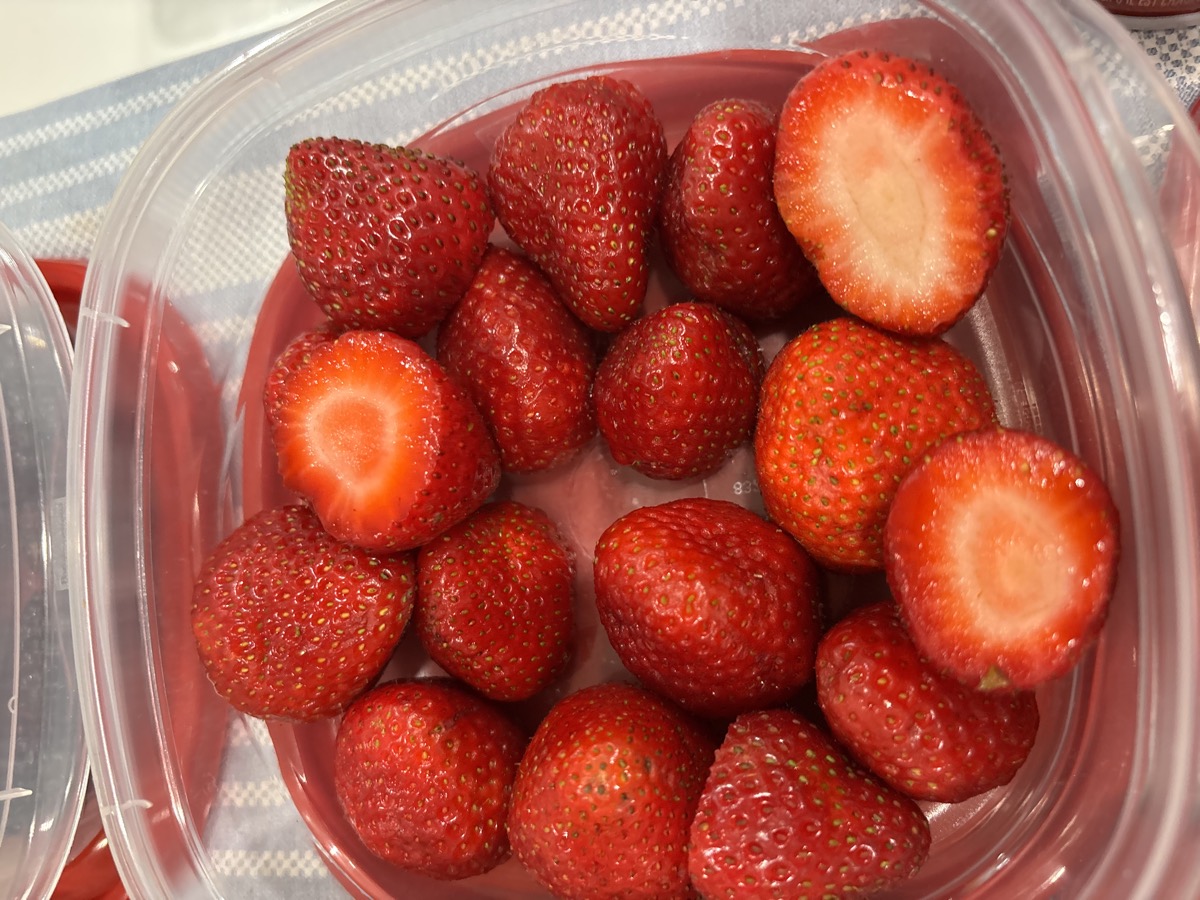 A container of fresh strawberries, some cut in half