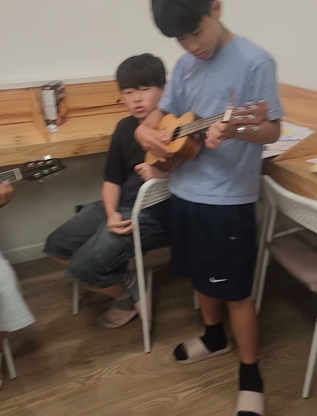 Two students playing ukulele and guitar together during the birthday celebration