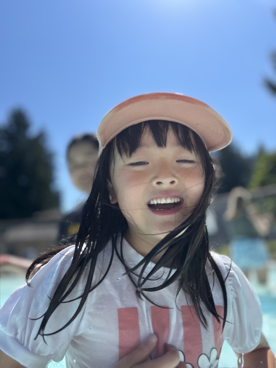 A camper laughing with wet hair against a bright blue sky at the pool