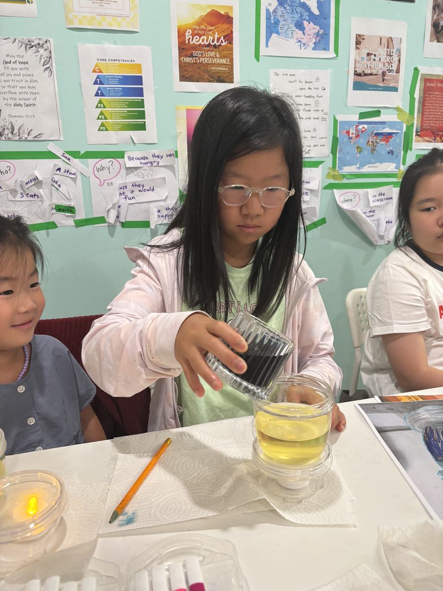 A group of students around the table pouring into their jars, a tea light glowing beside them