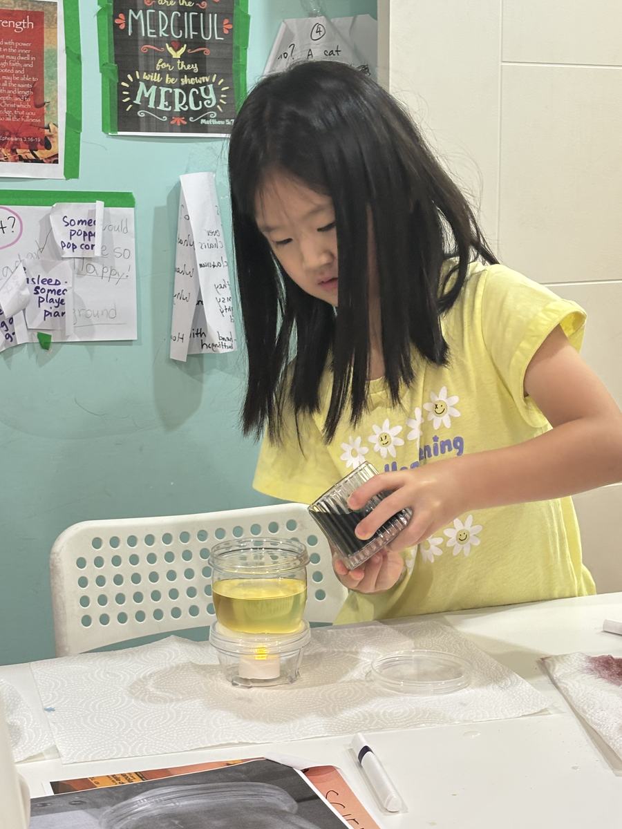 A student adding to her jar of yellow oil at the table