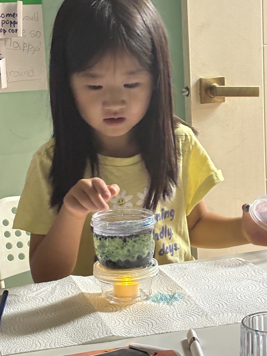 A young student reaching toward her green lava lamp glowing on the table