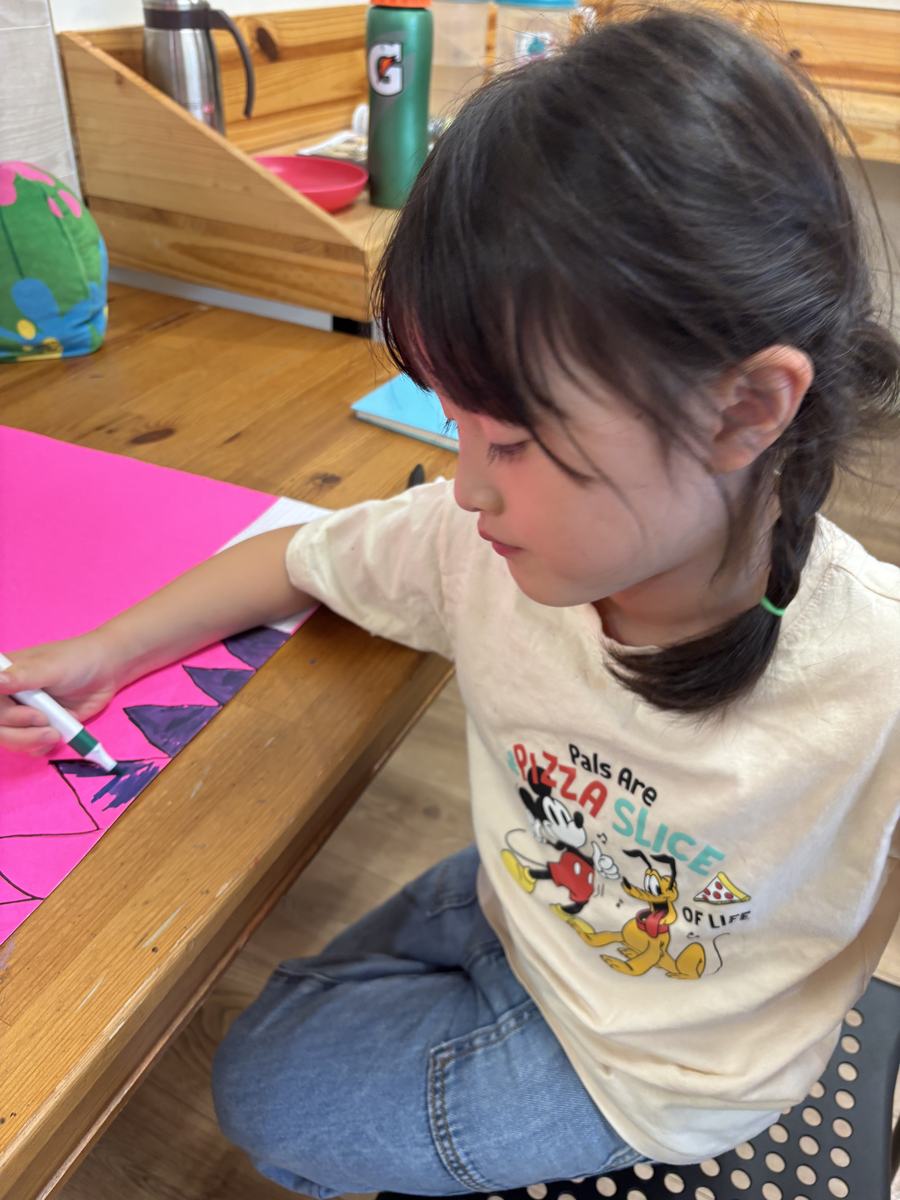 A younger student cutting shapes from bright pink card for her poster