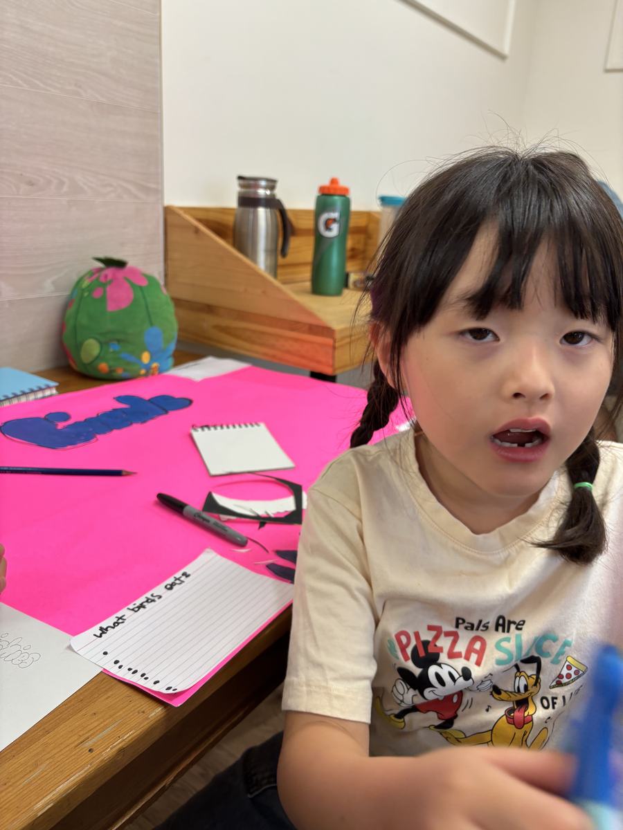 A student at the craft table with pink and blue card and her materials