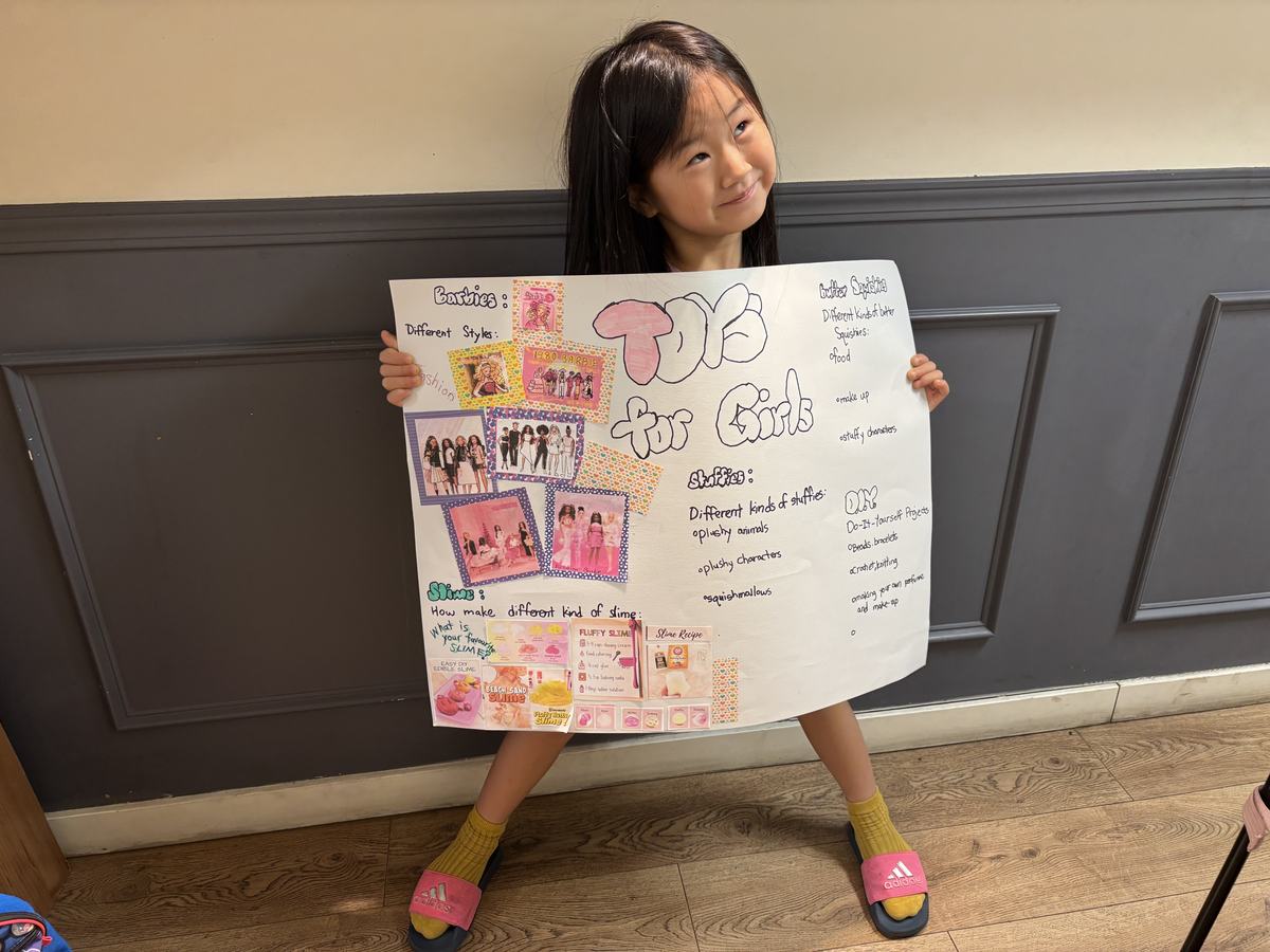 A student holding up her large poster titled Toys for Girls, divided into sections on Barbies, stuffies, squishies, DIY and slime with magazine cutouts