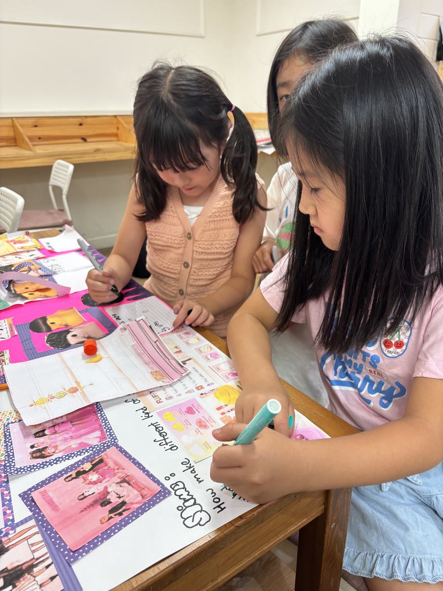 Students writing and colouring on their poster together at the table