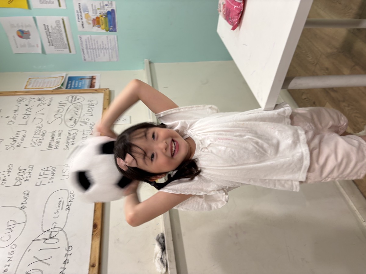 A little girl smiling brightly with a plush soccer ball on her head