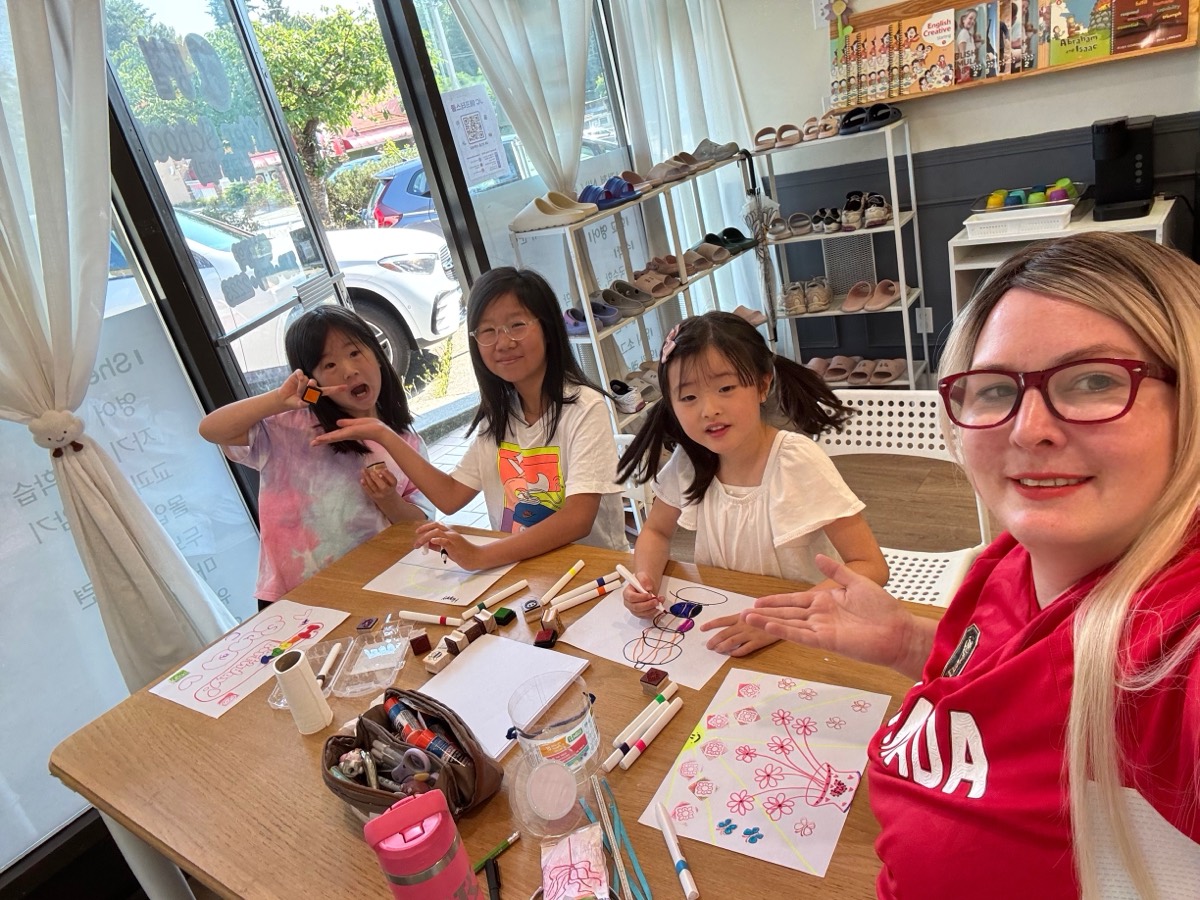 Ms. Diane smiling at the craft table with three girls drawing with markers and stamps