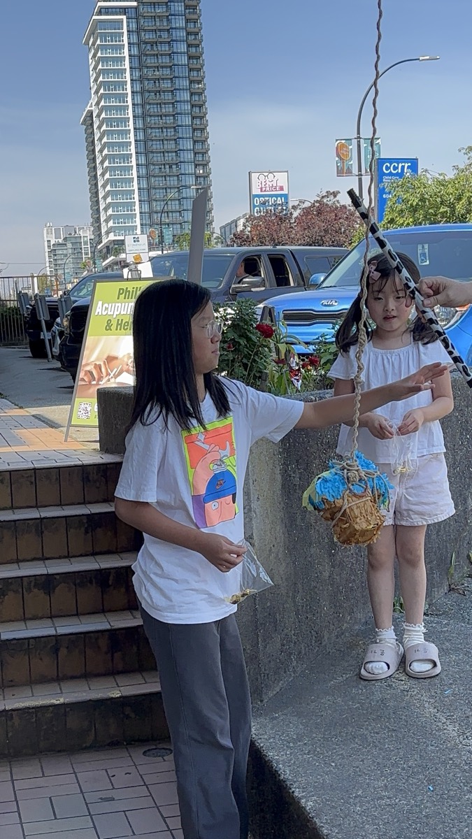 An older student helping a younger girl with the candy basket outside