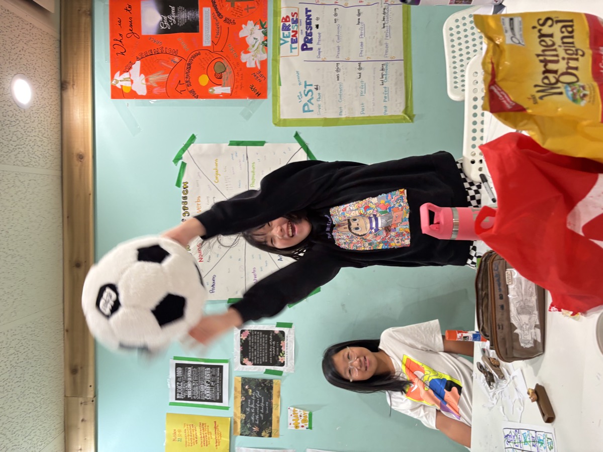 A girl joyfully raising the plush soccer ball above her head in front of the class