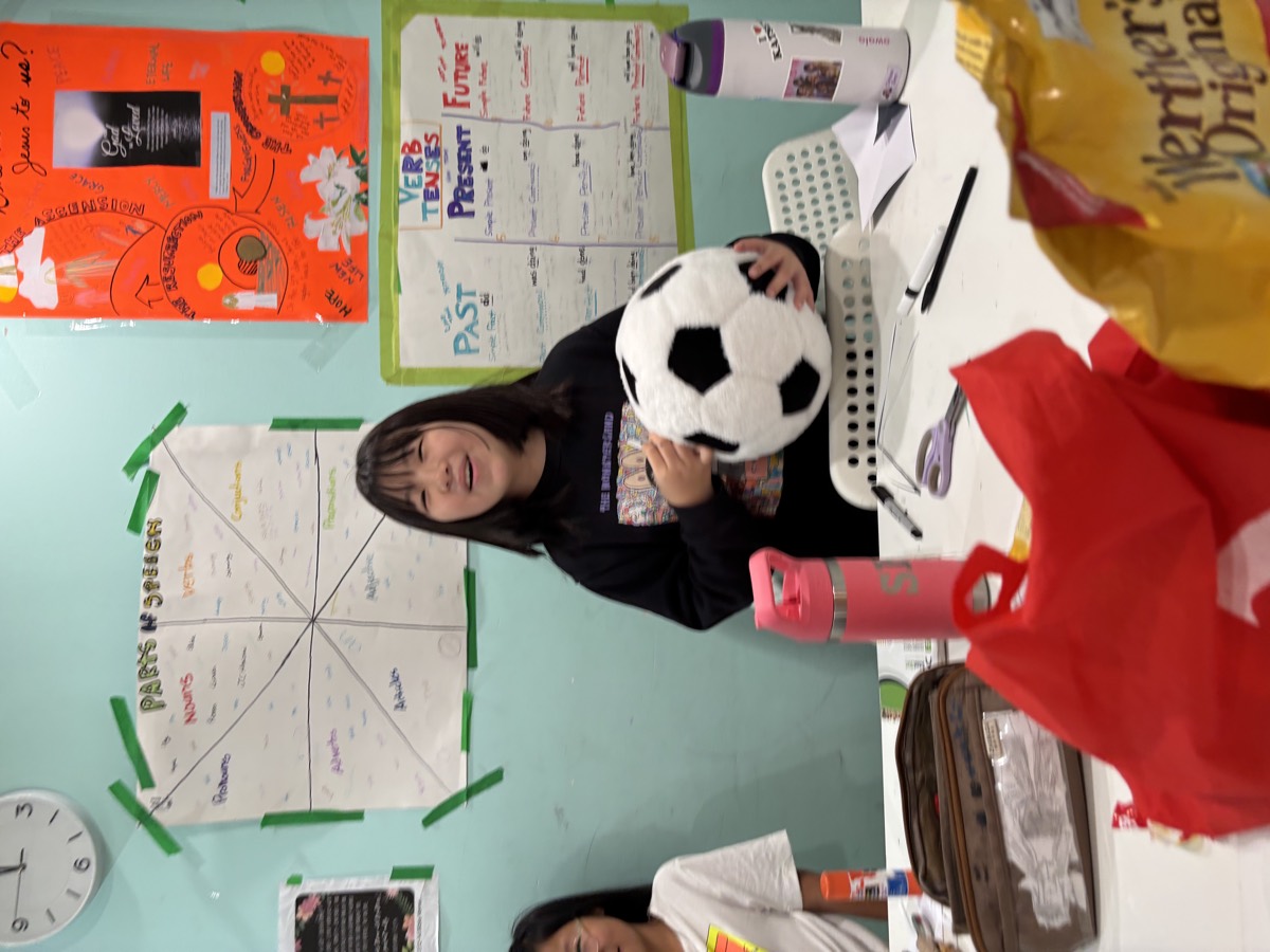 A girl holding the soccer ball while speaking in front of grammar posters