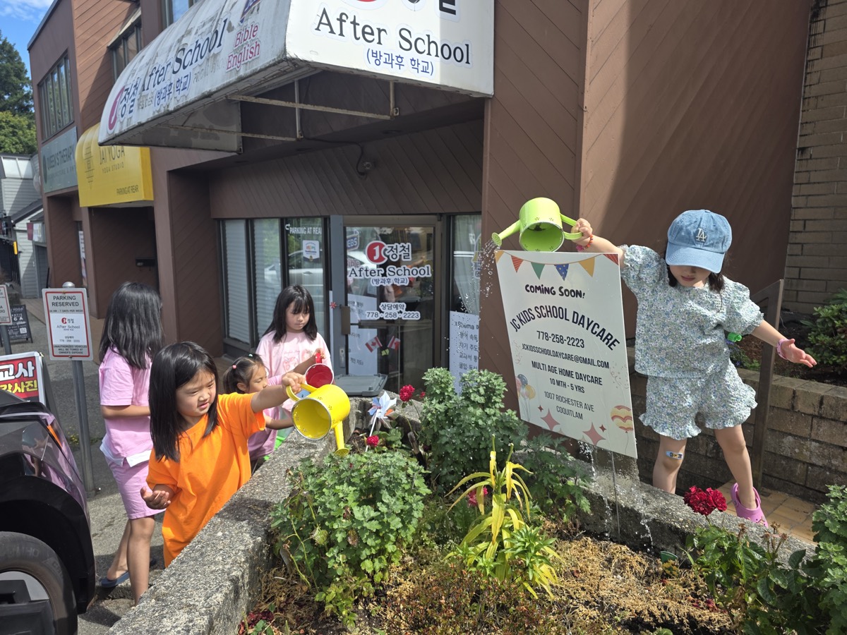 Kids with colorful watering cans tending the flowers in front of JC After School