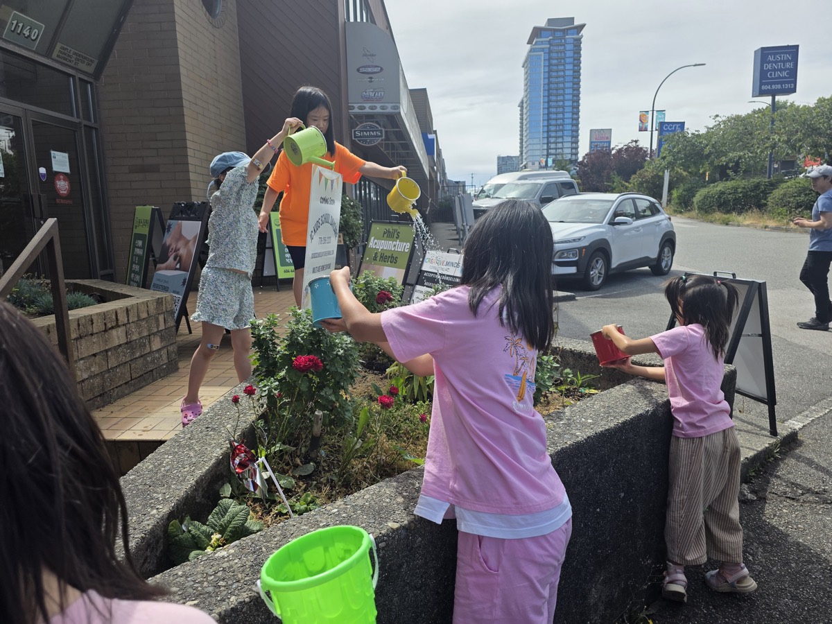 Children watering the flower planter together outside the school
