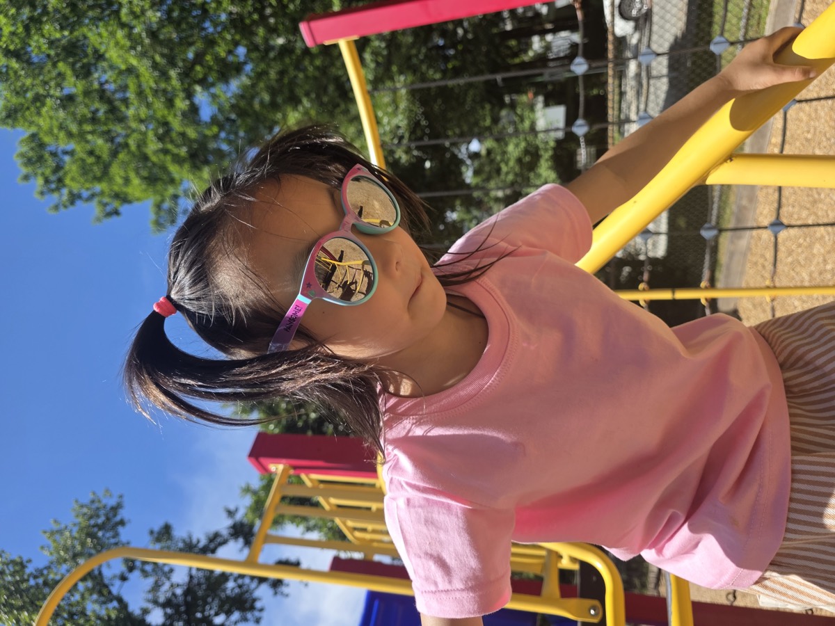 A girl in sunglasses climbing at the playground