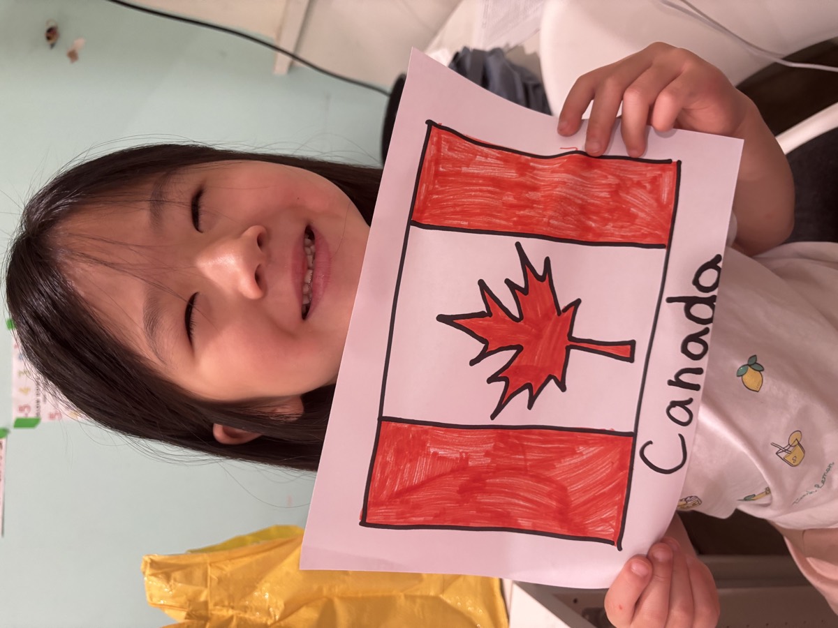 A girl smiling and holding her hand-colored Canada flag drawing