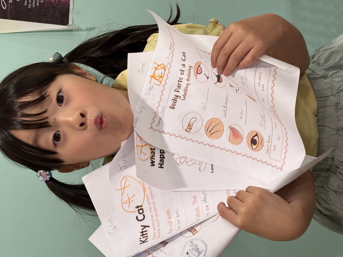 A student making a silly face while holding up her finished Kitty Cat worksheets