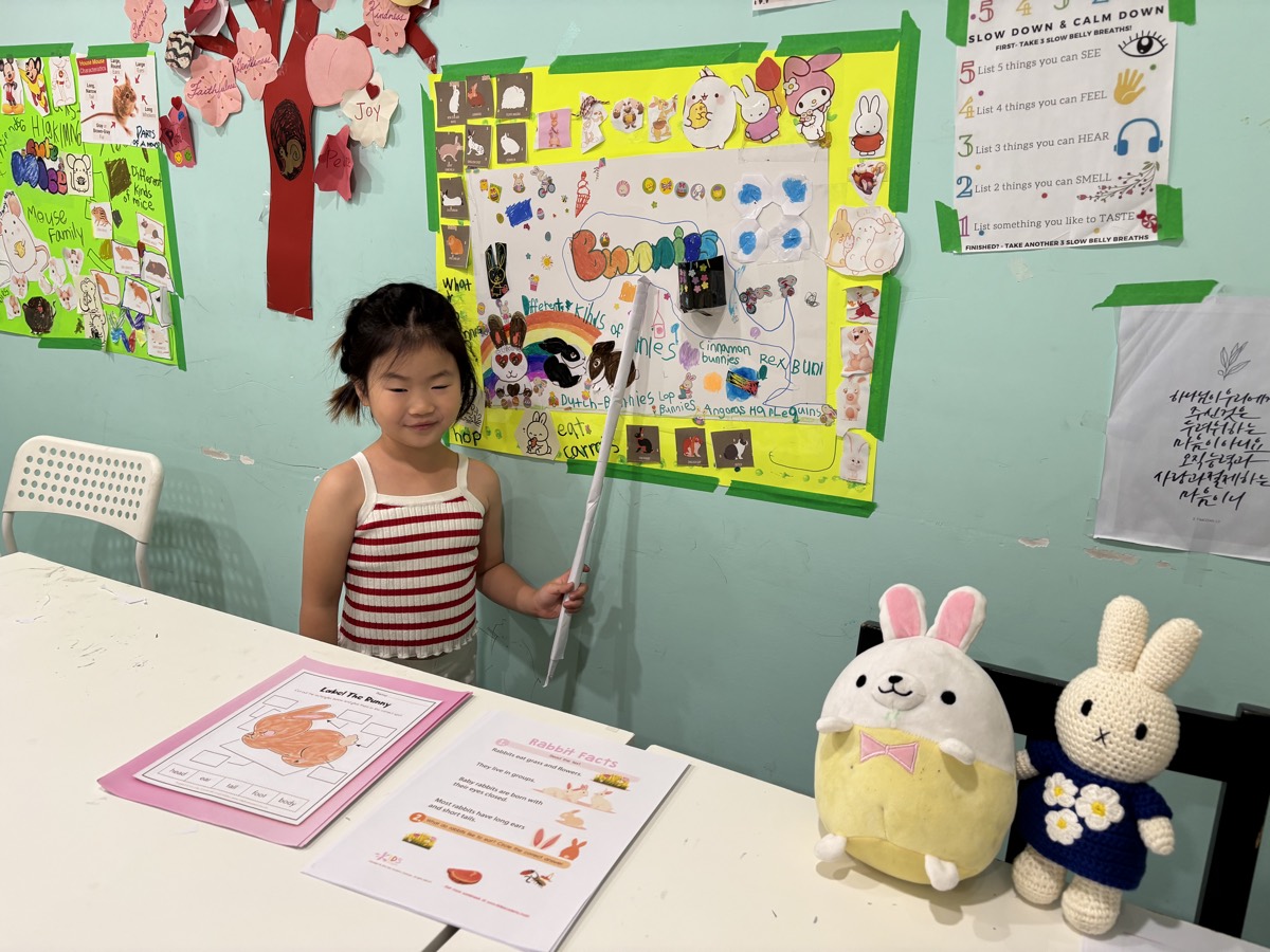 SueAh presenting her Bunnies poster with a pointer, bunny plushies beside her