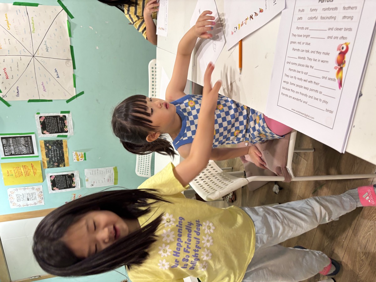 Sua leaning in to give a young student instructions on her bird worksheet