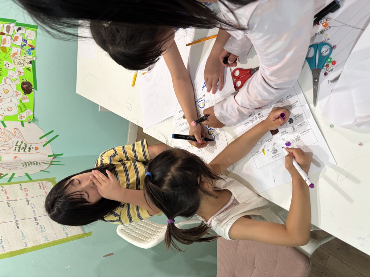 Loha guiding two young students as they colour their bubble tea worksheets with markers