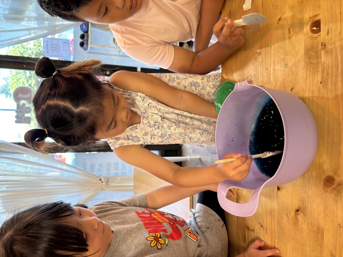 A girl stirring the bowl of jelly with a wooden stick while friends watch