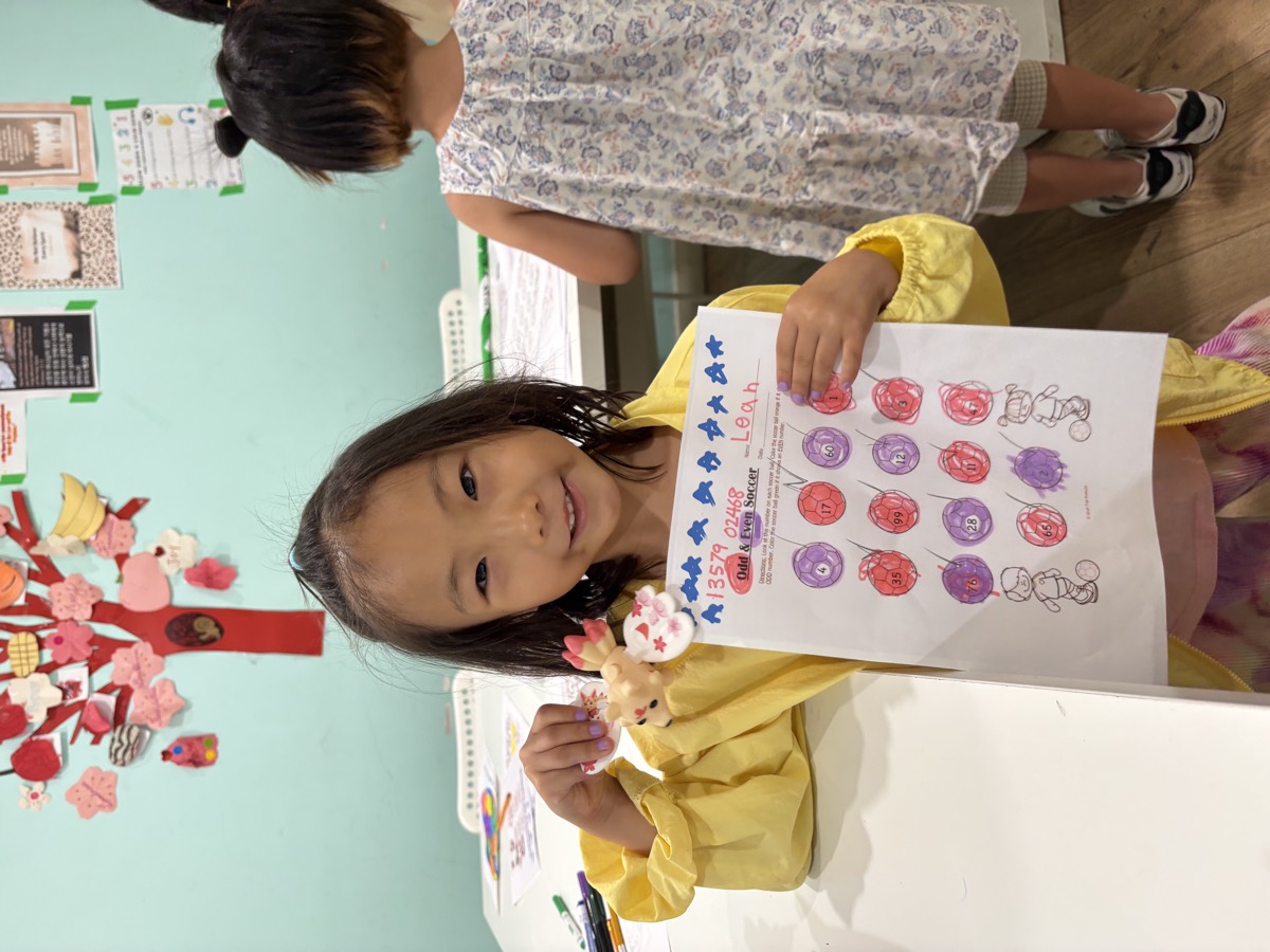 Leah smiling and proudly holding up her completed Odd and Even Soccer worksheet decorated with stars and bows