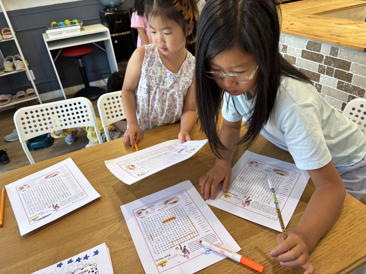 An older student helping a younger one with a soccer word-search worksheet