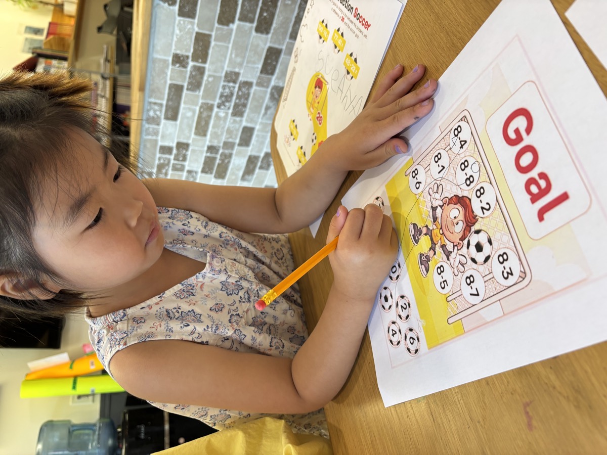 A young student concentrating on a Goal soccer math worksheet with a pencil