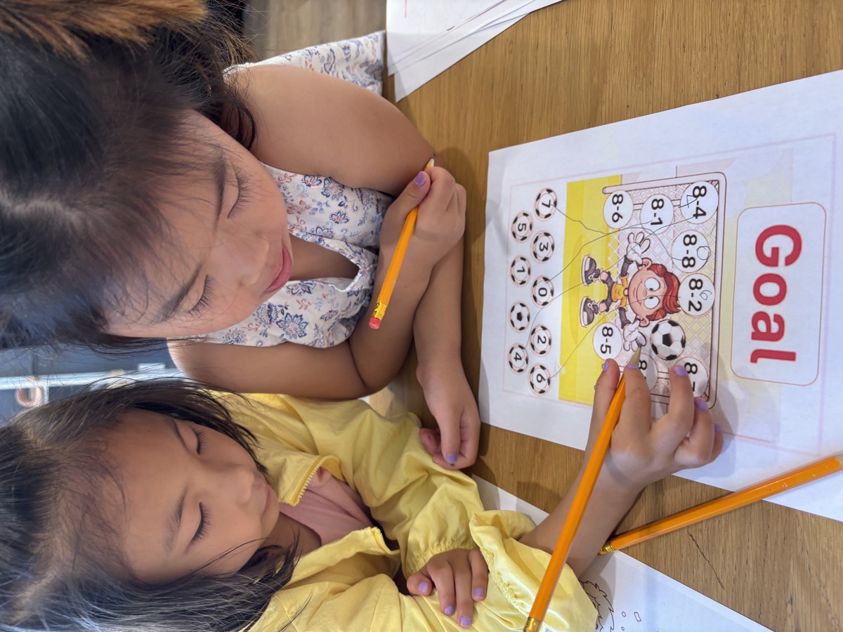 Two girls working side by side on the same soccer math worksheet