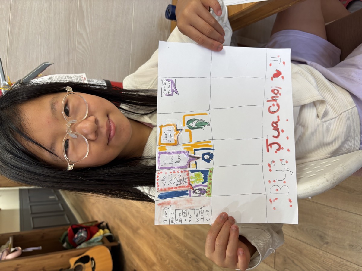 An older student holding up her multi-panel comic strip dialogue signed By Jua Cho