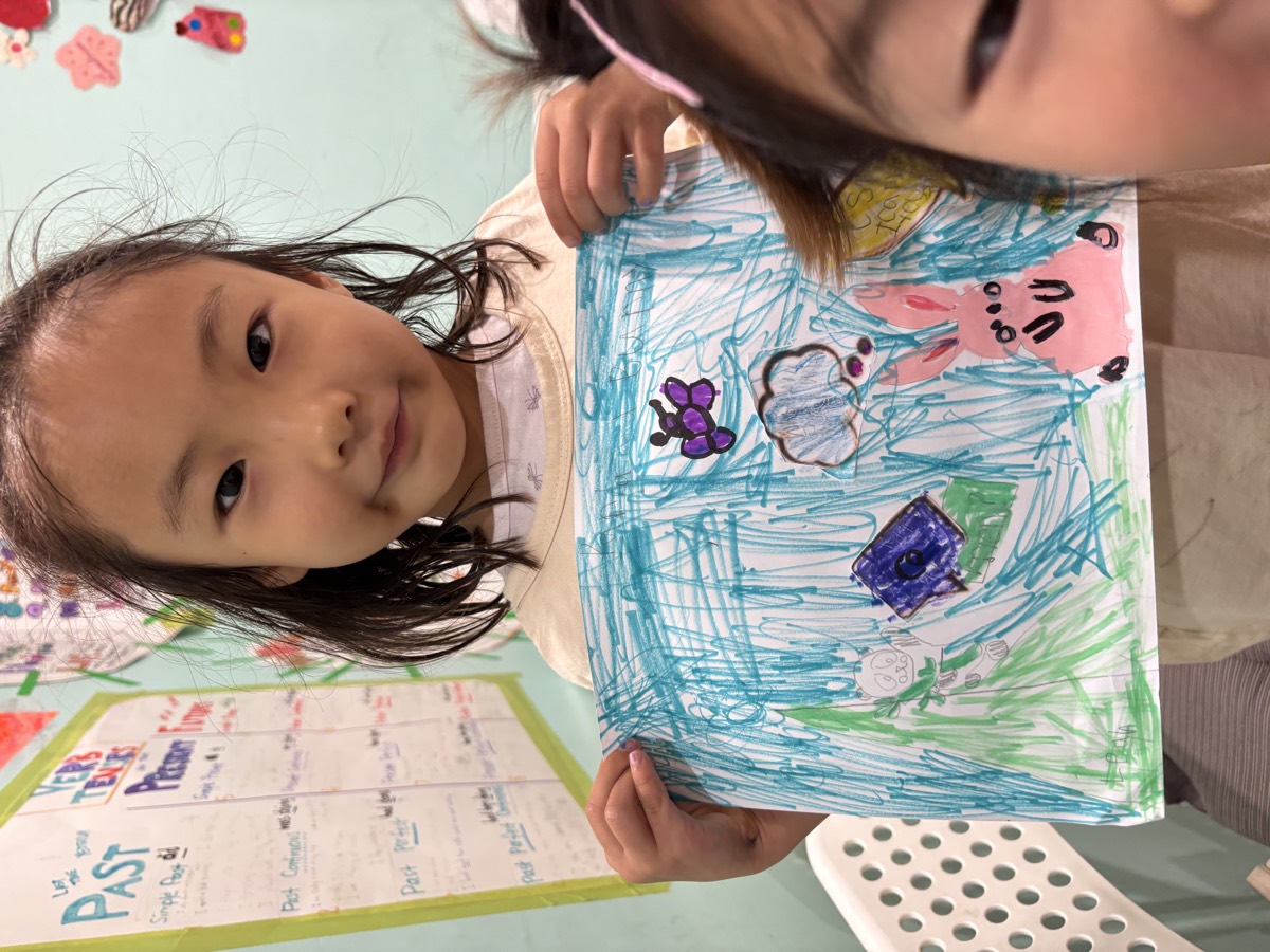 Two students smiling and holding up a blue crayon drawing with speech bubbles
