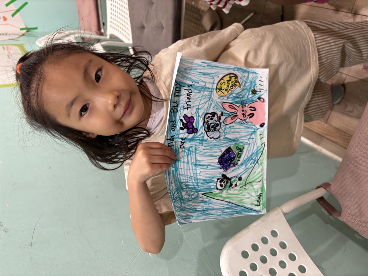 A student holding her illustrated dialogue drawing of animals who are best friends