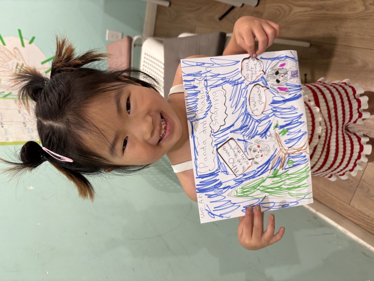 A student holding up her drawing titled Panda and Rabbit Sharing with speech bubbles