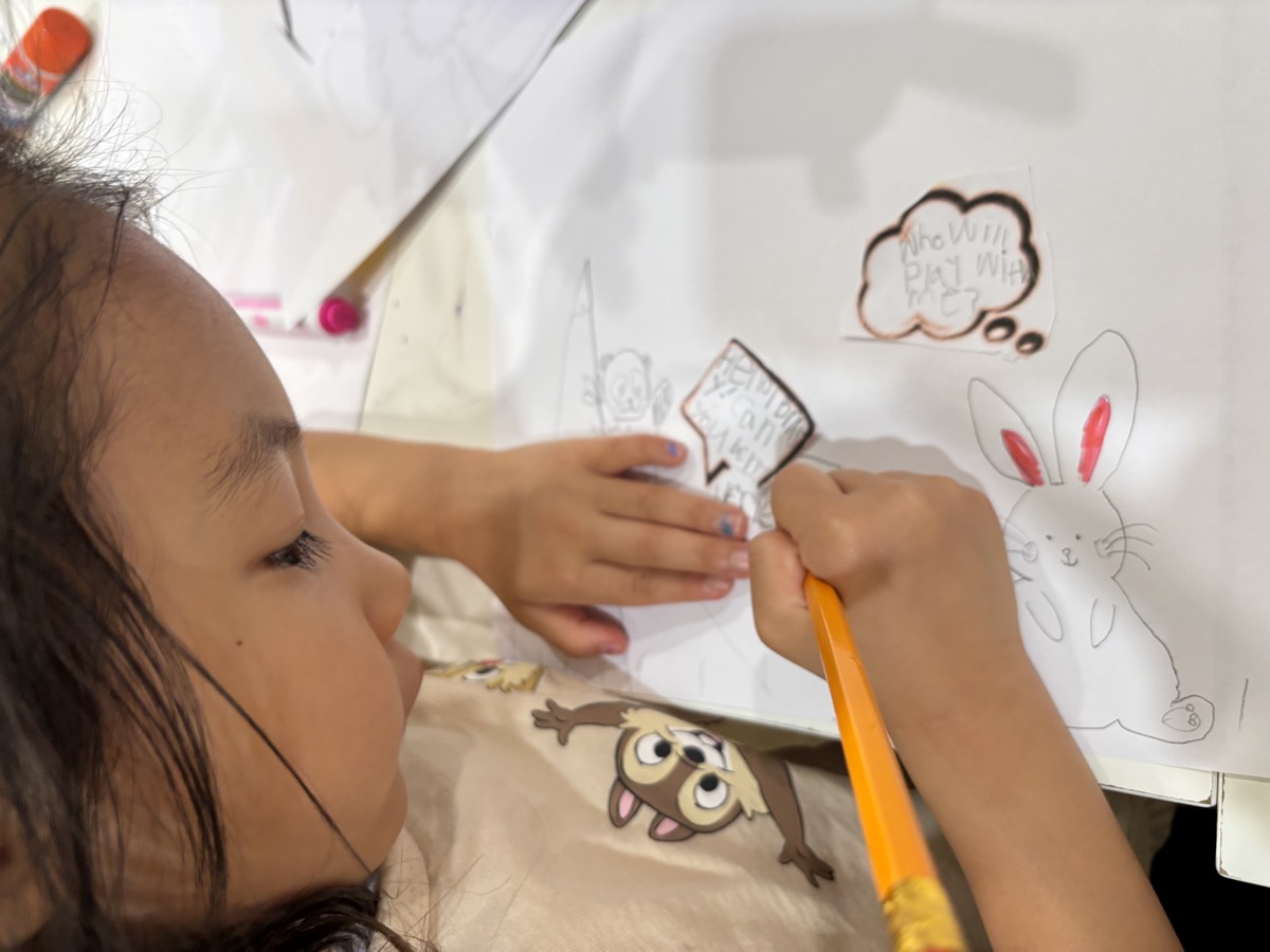 A student carefully colouring in a speech bubble above her pencil drawing