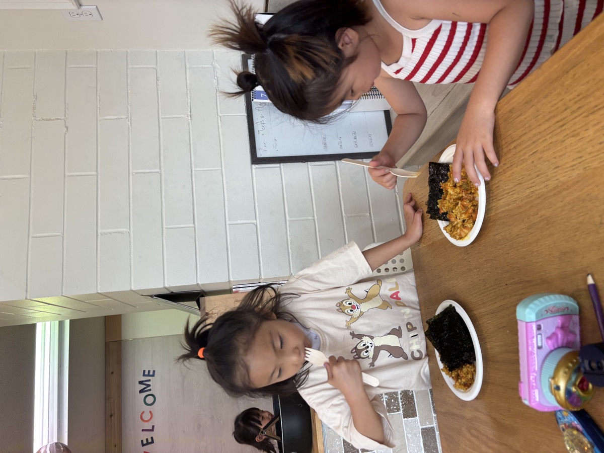 Two young students eating plates of kimchi fried rice with seaweed at the table