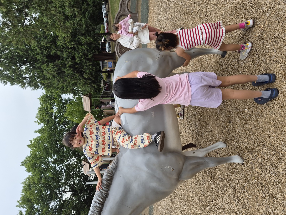 Children climbing on and gathered around the grey horse statue at the park