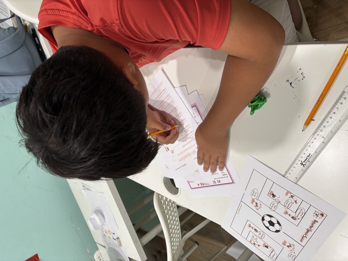 Minwoo working through Wh-Questions and Reported Speech Soccer worksheets at his desk