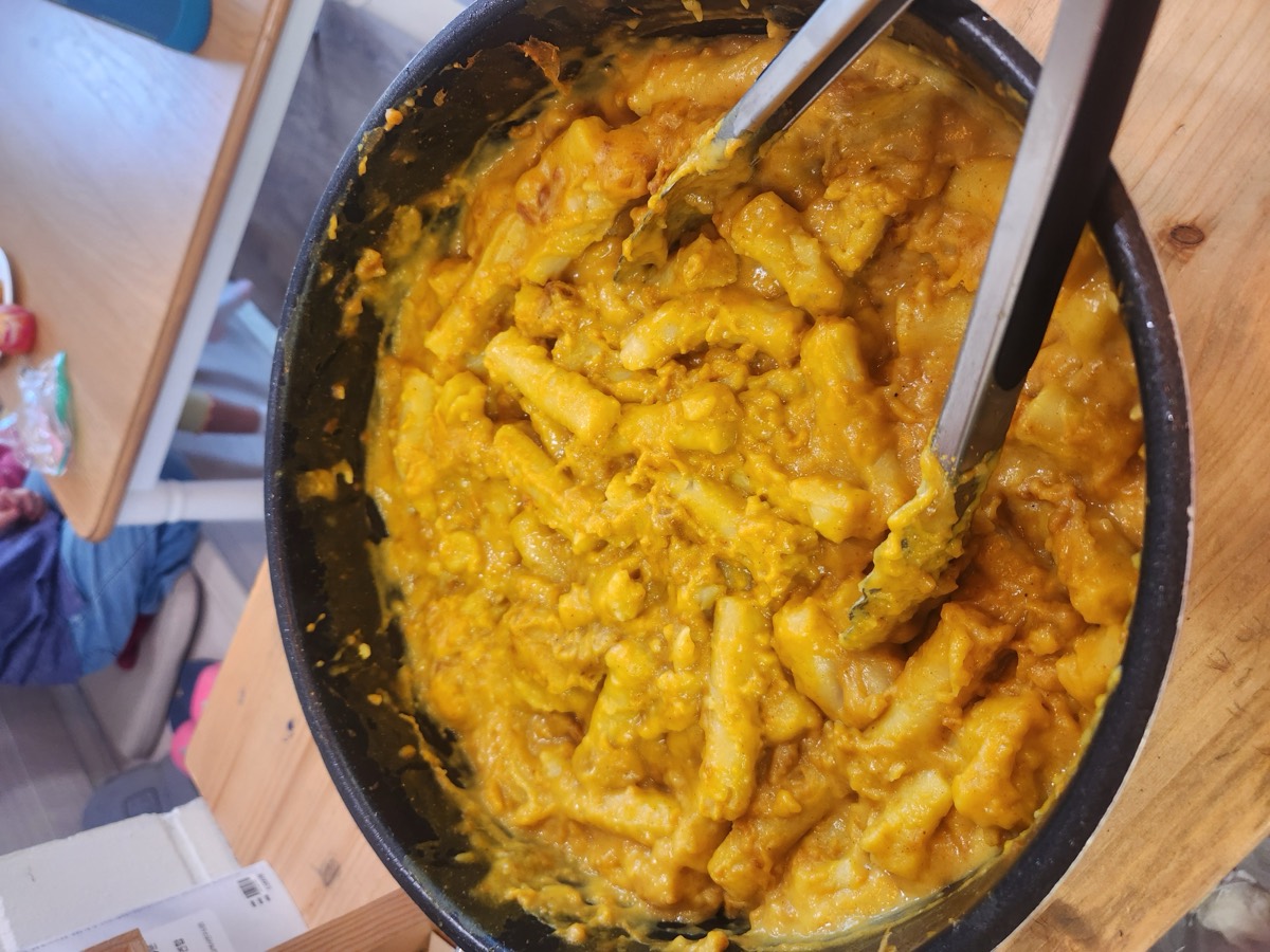 A big pot of curry-coated tteokbokki rice cakes with tongs resting inside