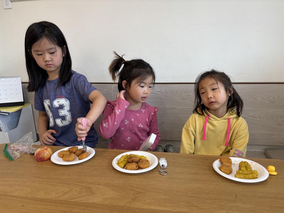 Three students sitting at the table eating their plates of curry tteokbokki and croquettes