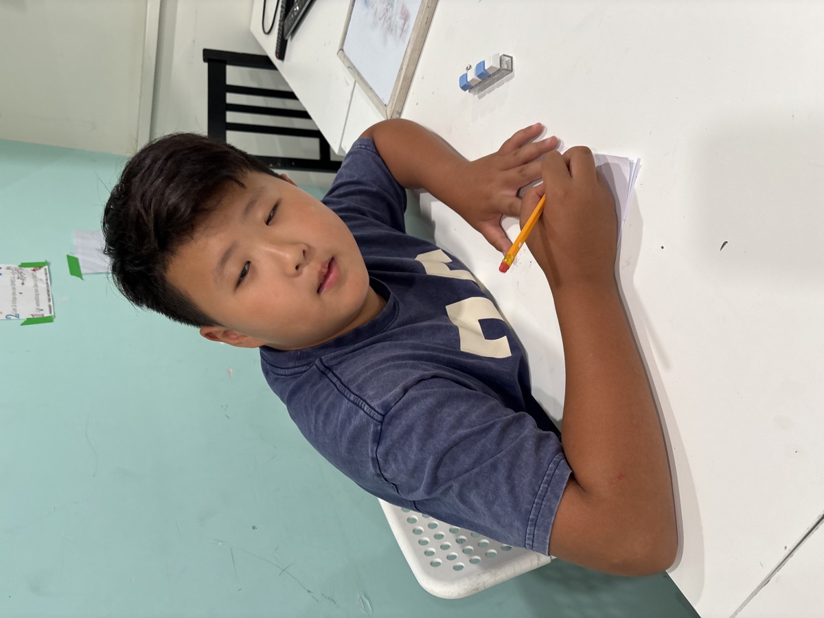 An older student in a navy shirt concentrating as he writes with a pencil at his desk