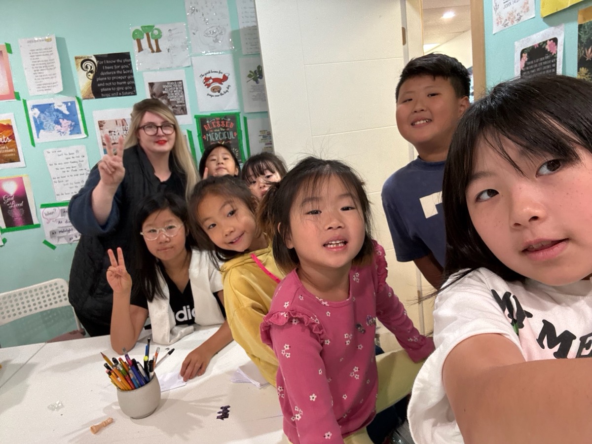 A cheerful group selfie of the teacher and the whole class making peace signs in front of the classroom wall
